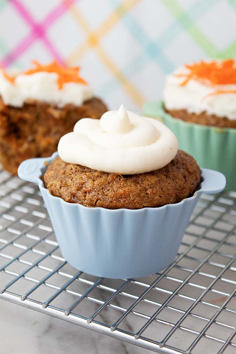 sideview of carrot cake cupcakes with cream cheese frosting on a cooling rack
