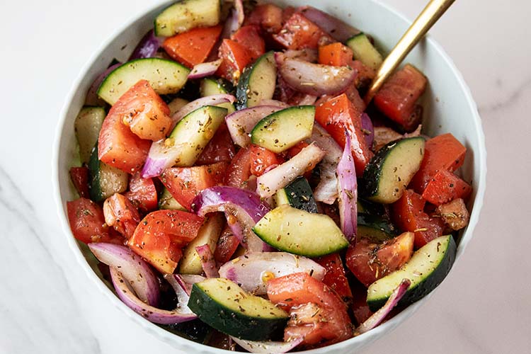 overhead view of cucumber and tomato salad ready to be served with a gold spoon