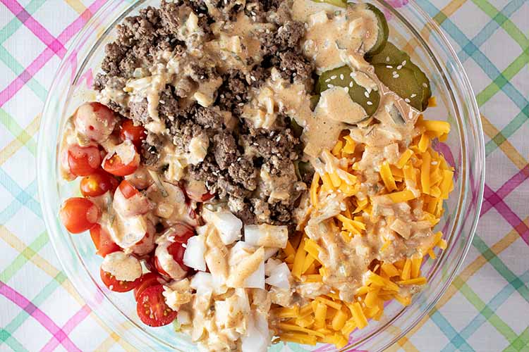 overhead view of Big Mac salad ingredients evenly spaced in a glass bowl and topped with Big Mac sauce and ready to be tossed