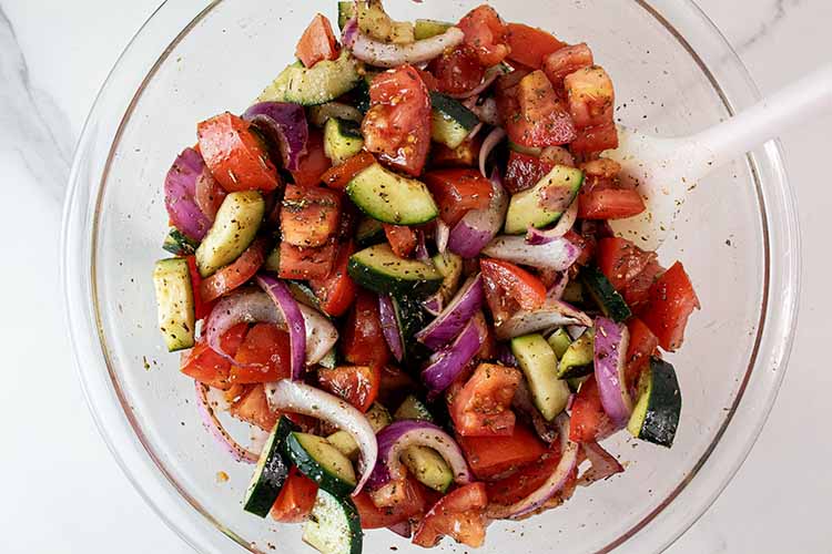 overhead view of vegetables lightly tossed with dressing in glass mixing bowl