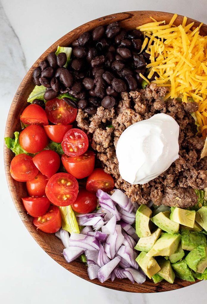 overhead view of taco salad in a serving bowl with each ingredient evenly spaced around and ready to be tossed and served