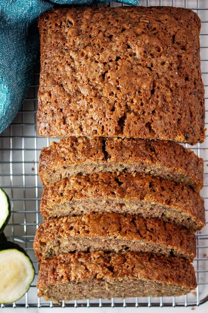 overhead view of loaf of cooled zucchini bread on a wire rack with four slices cut