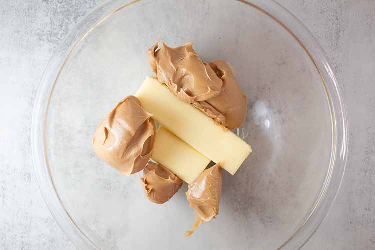 overhead view of peanut butter and butter added to a glass mixing bowl ready to be combined