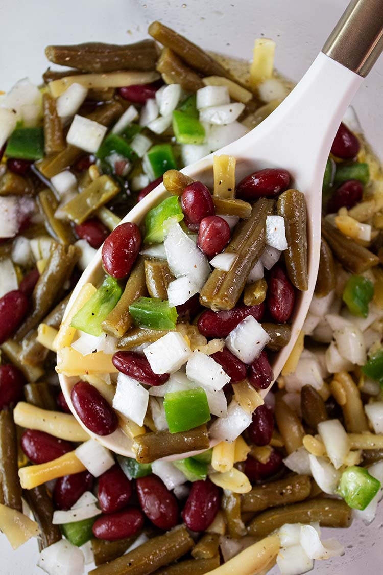 overhead view of three bean salad ready to serve with a white ladle removing a portion size