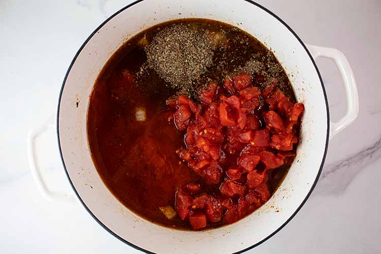 overhead view of cooking pot with tomatoes, broth and seasoning added and ready to cook