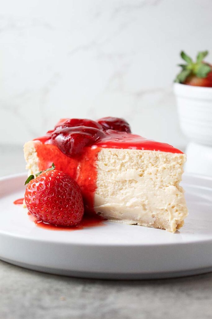 sideview of strawberry cheesecake topped with fresh strawberry topping on a serving dish